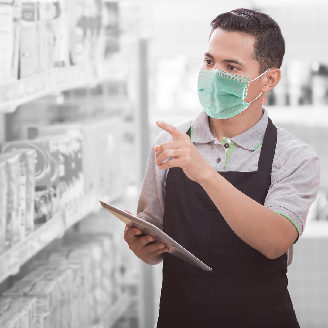 Pharmacist reviewing shelves with a mask over his mouth.